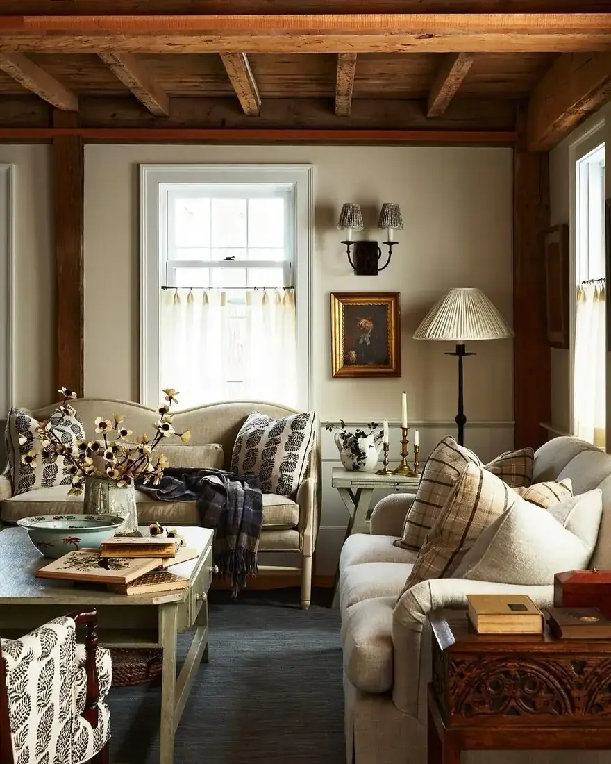 Two plain linen sofas facing under dark beams with cafe curtain and lamps