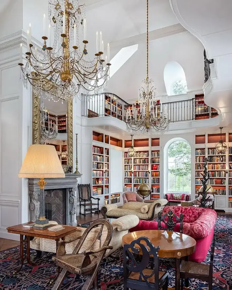 Double height white library with a marble fireplace, gilt mirror, and shelves running to a gallery