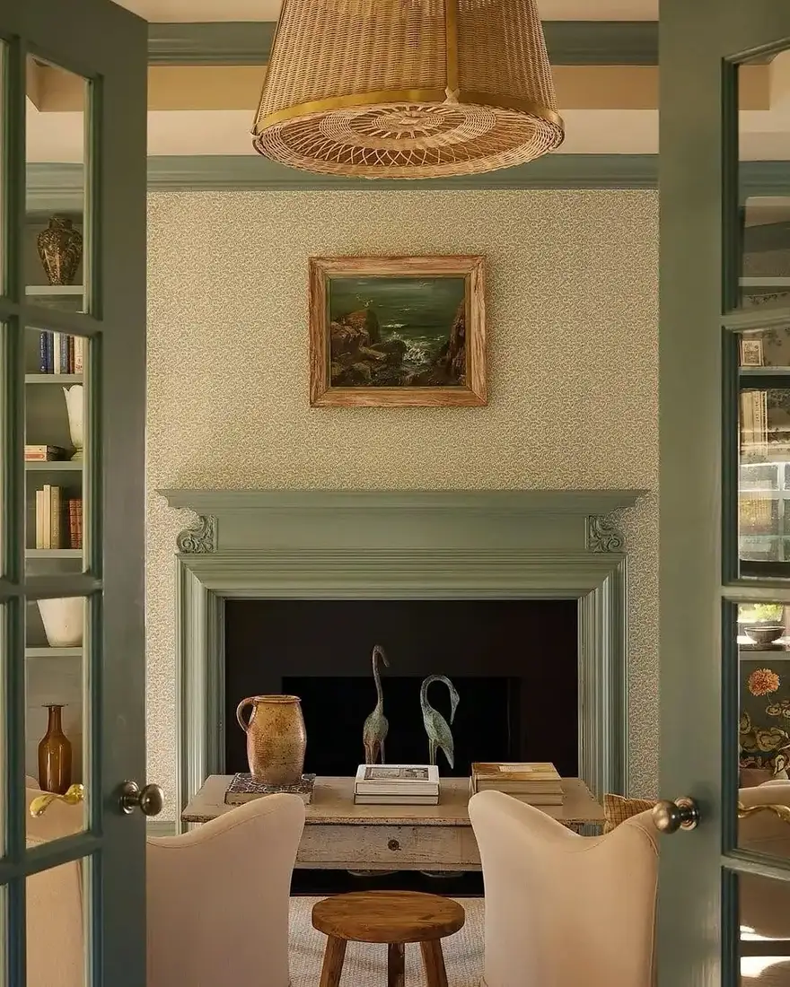 Sage green painted fireplace with an empty mantel shelf, a small seascape above and books and pottery on the hearth