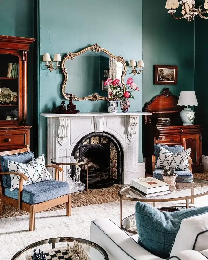 Teal panelled room with a white marble fireplace dressed with an ornate mirror, pink roses and dark glass