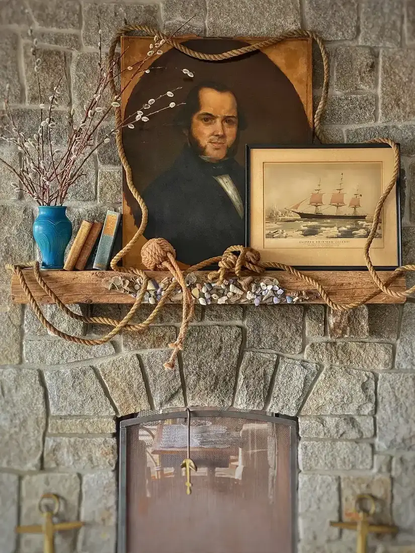 Close view of a stone mantel dressed with a portrait, a ship print, coiled rope and shells