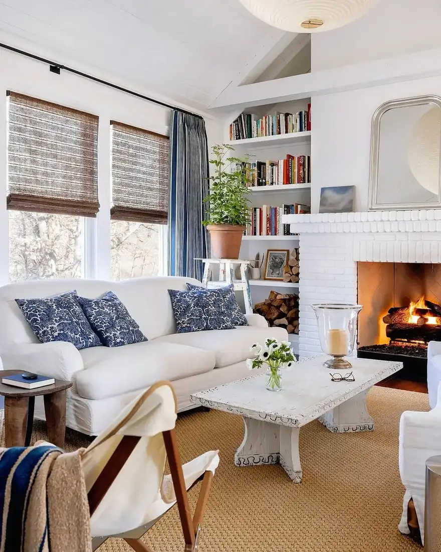 White painted brick fireplace with a lit fire, a leaning arch mirror and a small landscape on the mantel