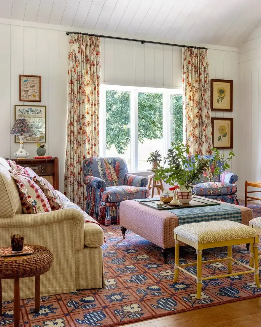 Floral sitting room with pink ottoman and layered cushions in soft daylight