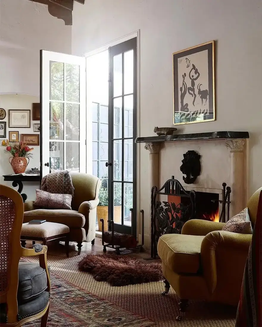 Two green velvet armchairs facing each other beside a lit limestone fireplace with a black slate shelf