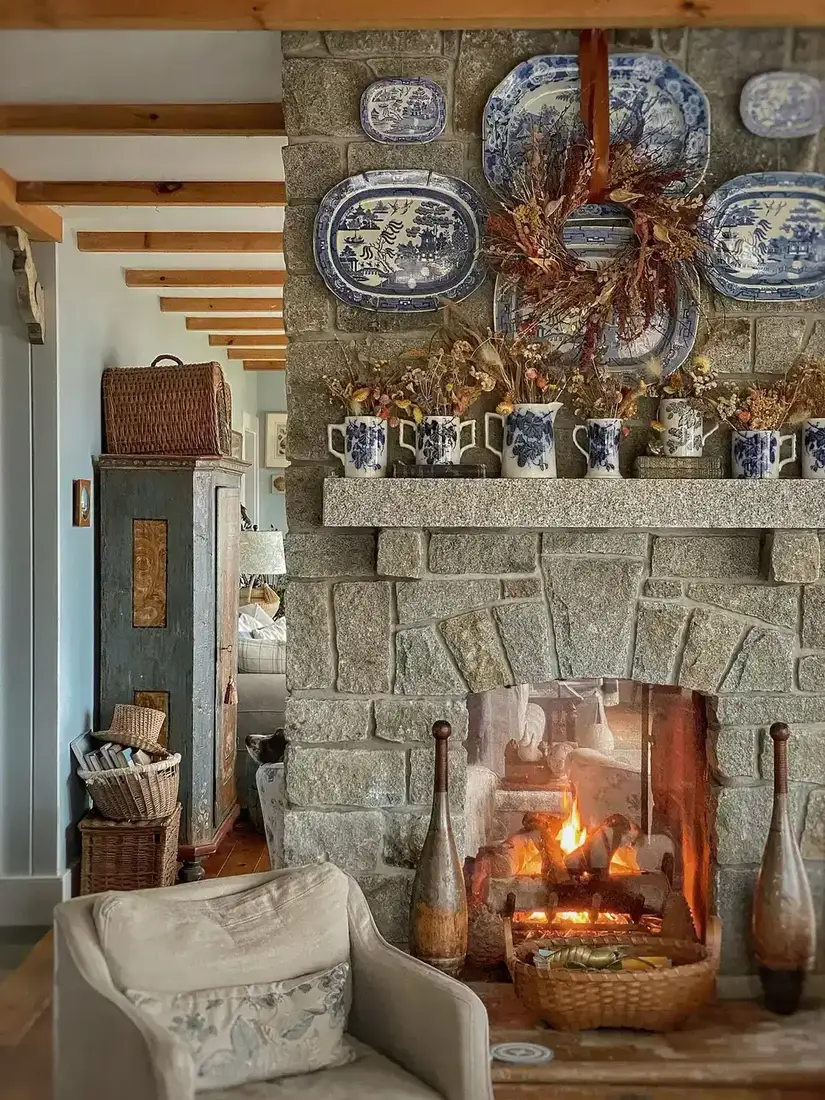 Granite fireplace with an arched firebox, transferware platters on the stone and a basket of birch logs