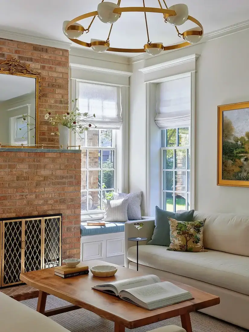 Unpainted red brick chimney breast with a gilt mirror above and a window seat between two sash windows