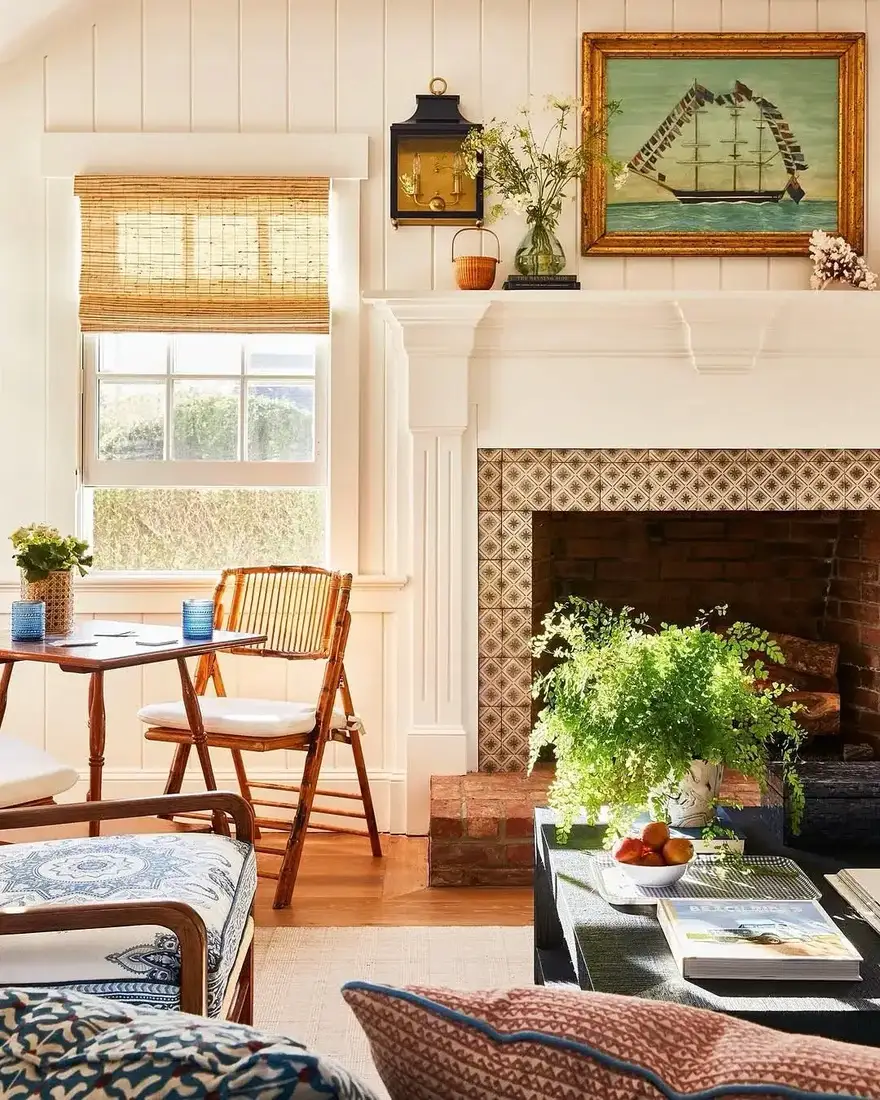 White panelled fireplace with geometric tile surround, black tole clock and a schooner painting in a sunlit room