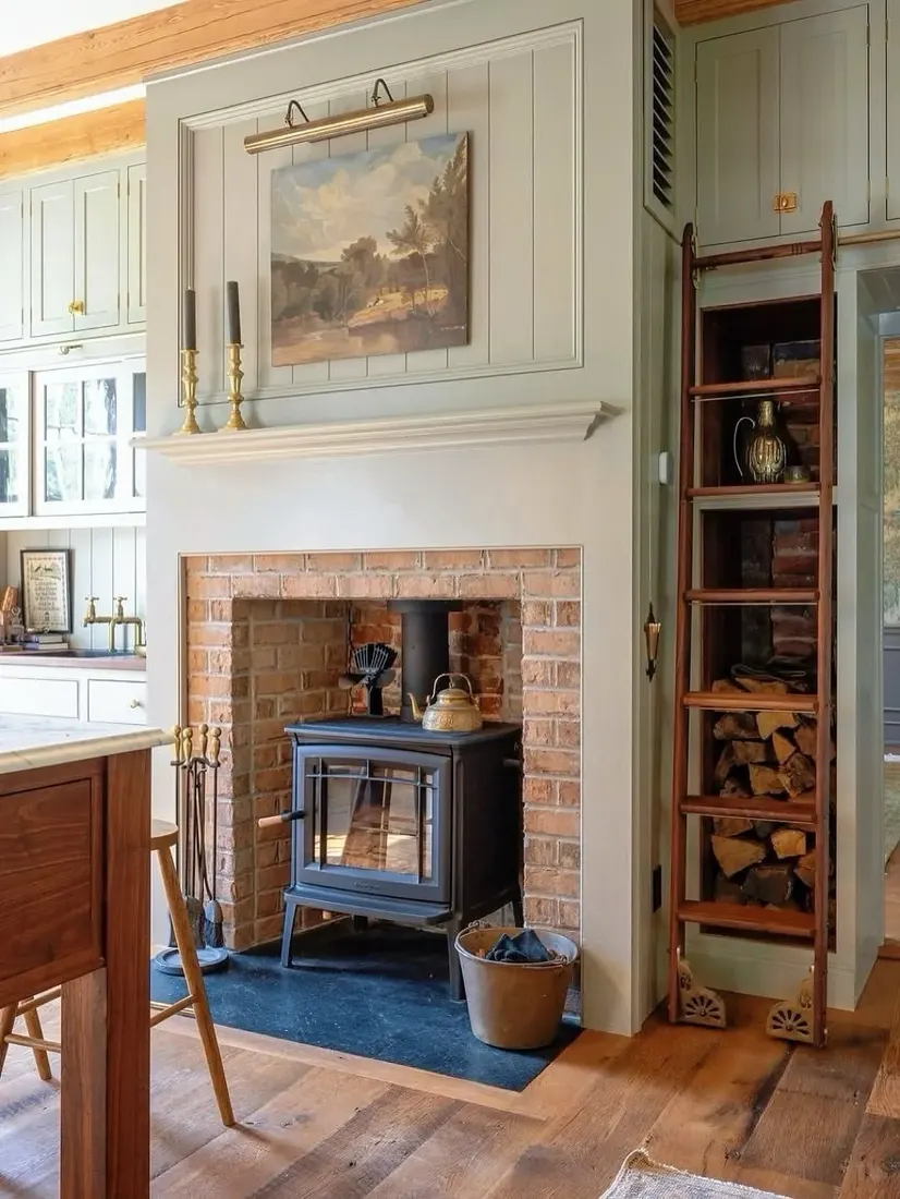 Black cast iron wood stove set into a brick alcove under a sage green panelled chimney breast