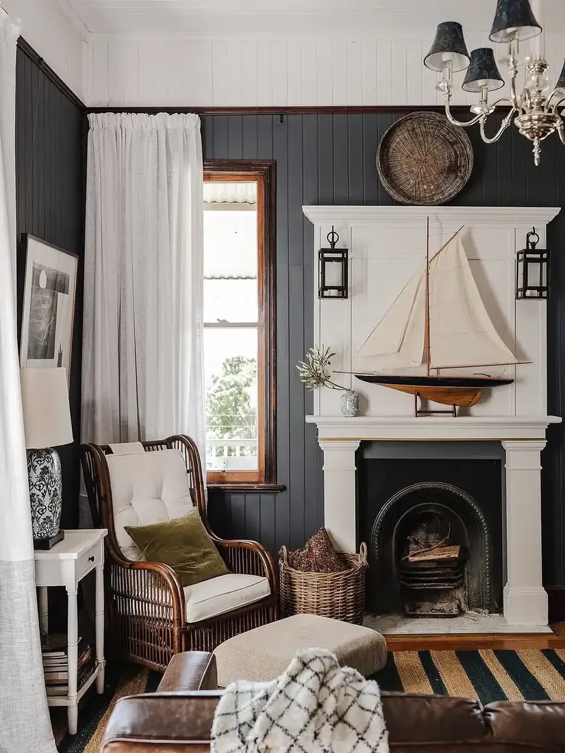 White mantel with a model sailboat against charcoal panelled walls with a rattan chair and striped rug