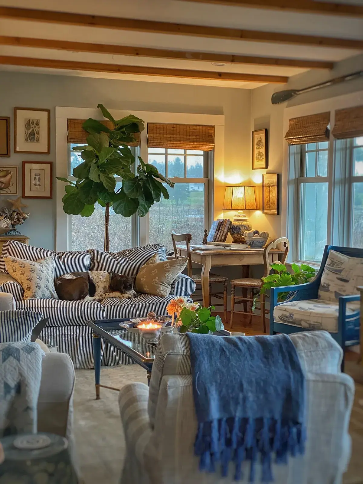 Living room at dusk with a ticking sofa, a lit table lamp and a blue painted armchair