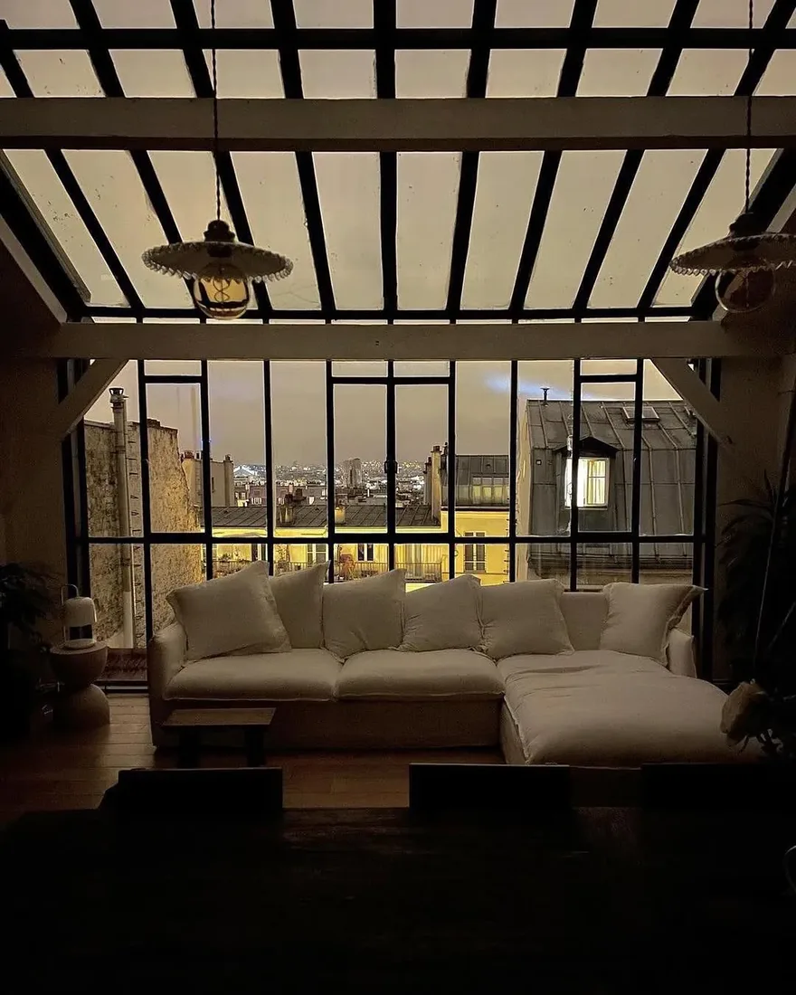 Paris loft at night with black steel glazing and deep linen sofa