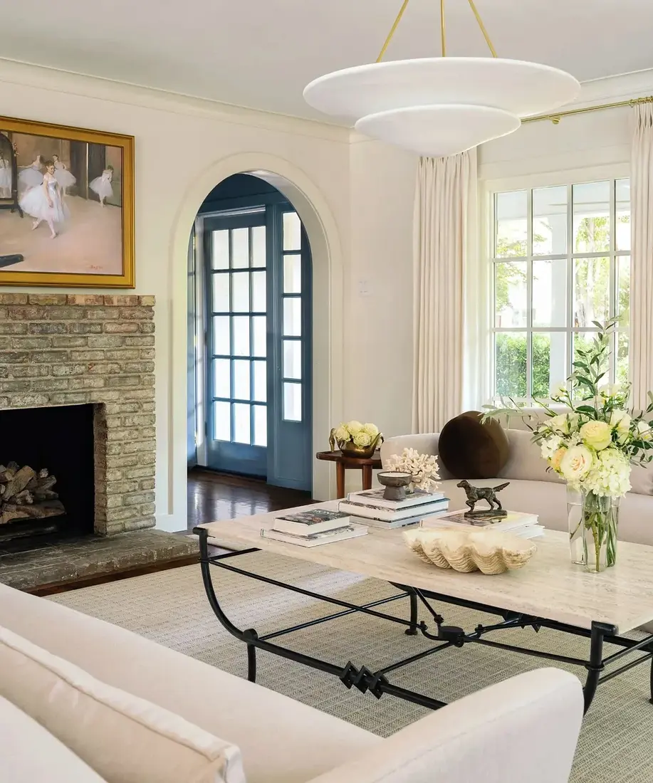 Pale brick fireplace with wide hearth, white sofas, stone topped table, gilt print above