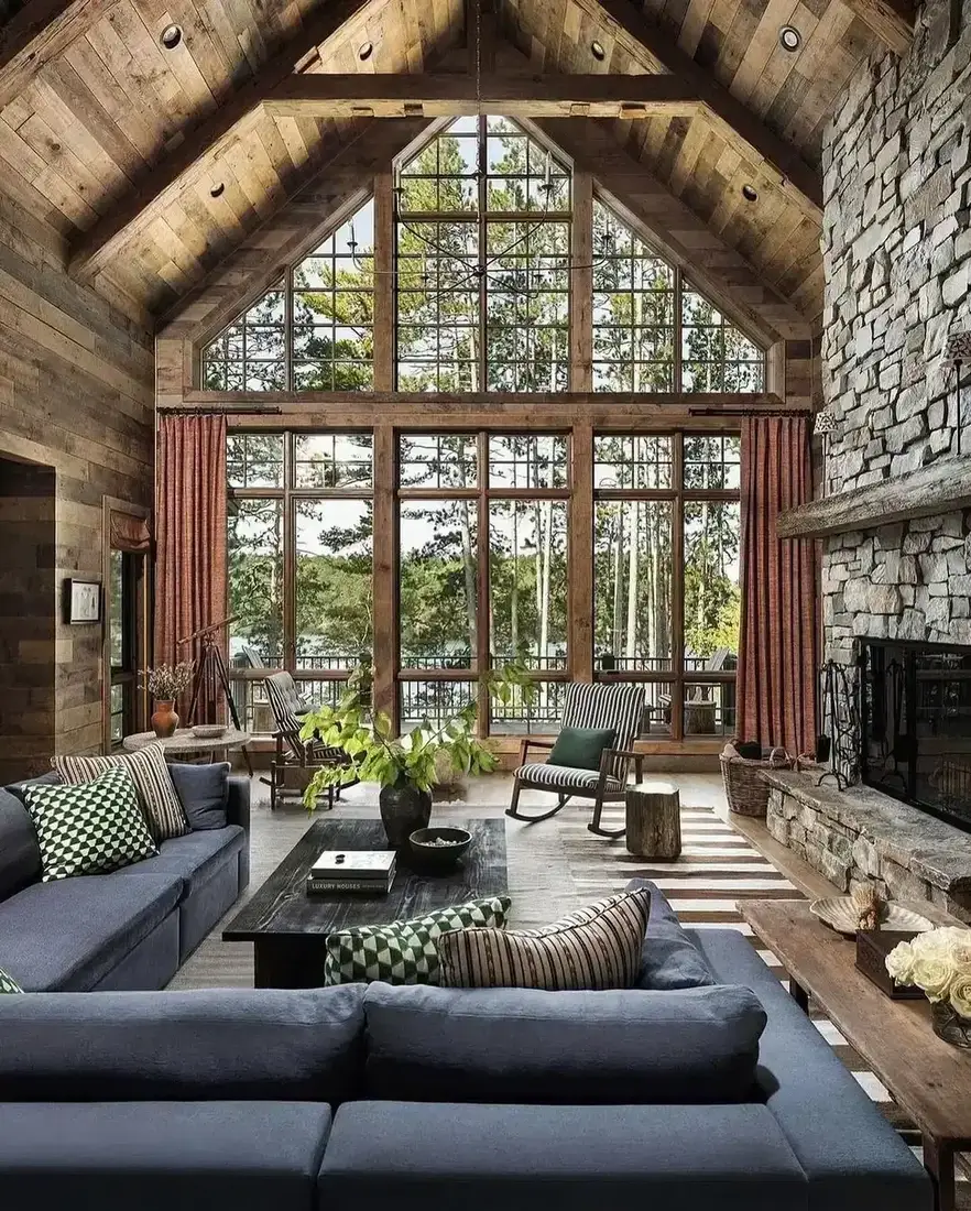 Full height grey rubble stone fireplace with timber mantel in a timber cabin, ink blue sofas, glazed gable