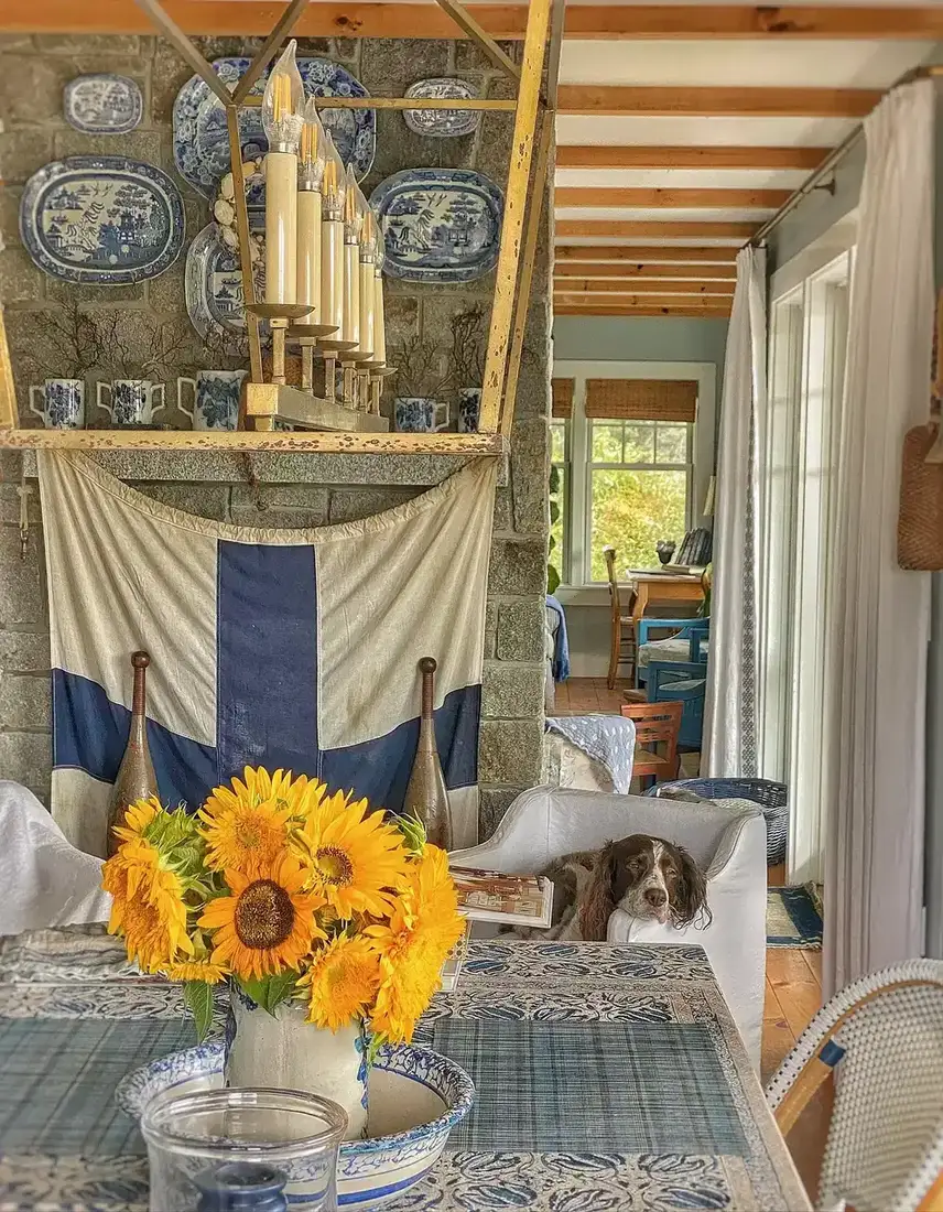 Grey granite fireplace behind a dining table with sunflowers, striped cloth over the mantel, cage pendant above