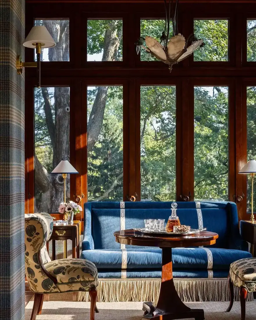 Blue velvet sofa with white tape and fringe set against dark timber windows