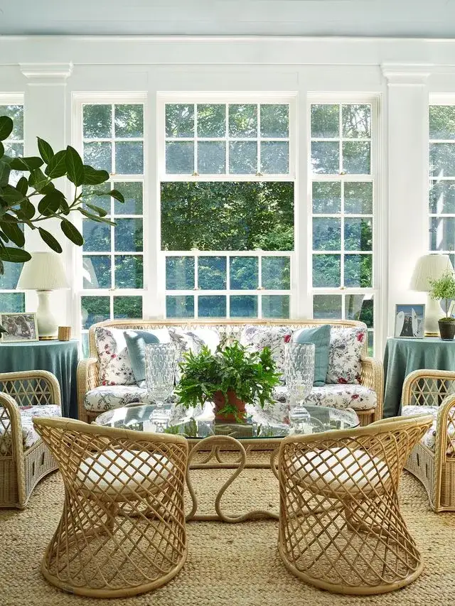 White sunroom with cane barrel chairs, floral sofa, and tall glazing