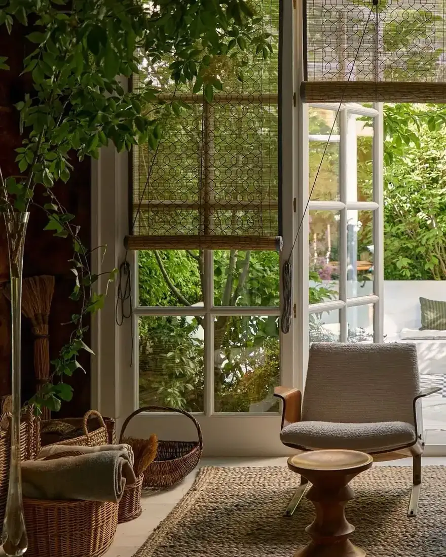 Glass doors with half lowered woven blind beside a bouclé chair and jute rug