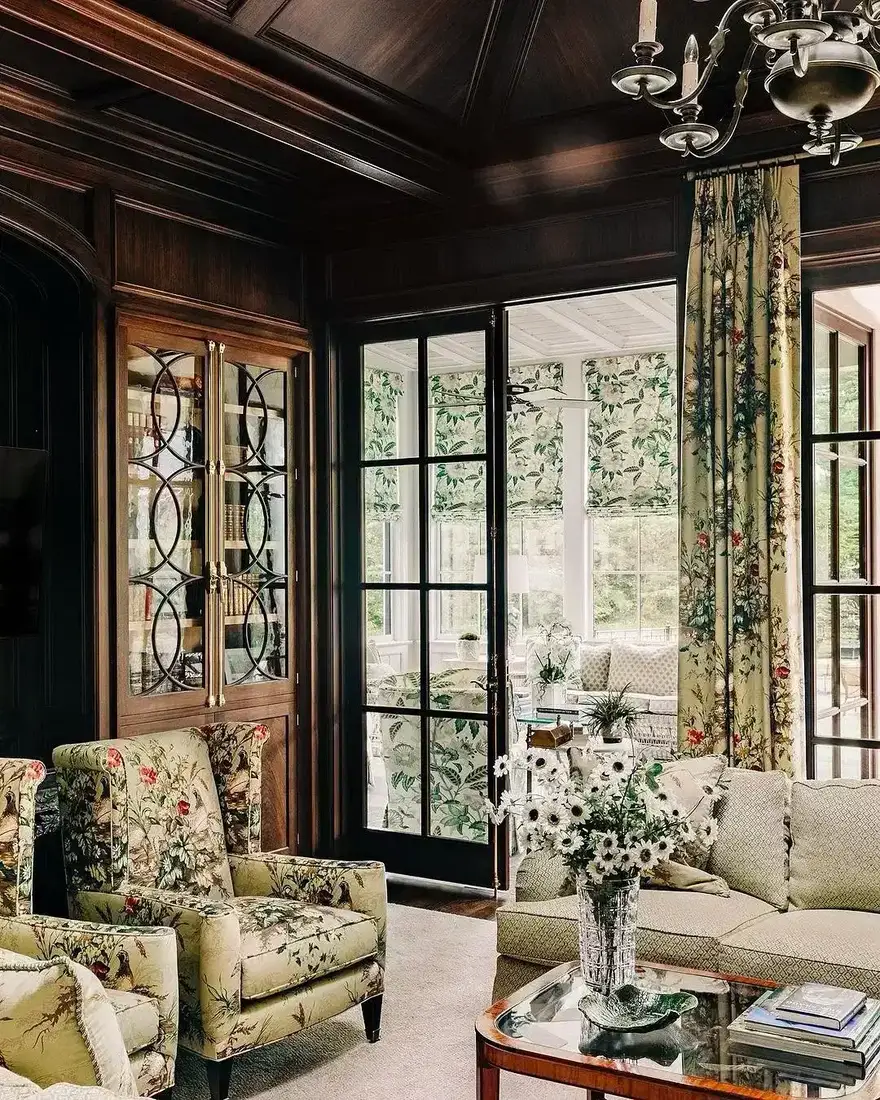 Dark panelled sitting room with chintz chairs opening to a bright orangery