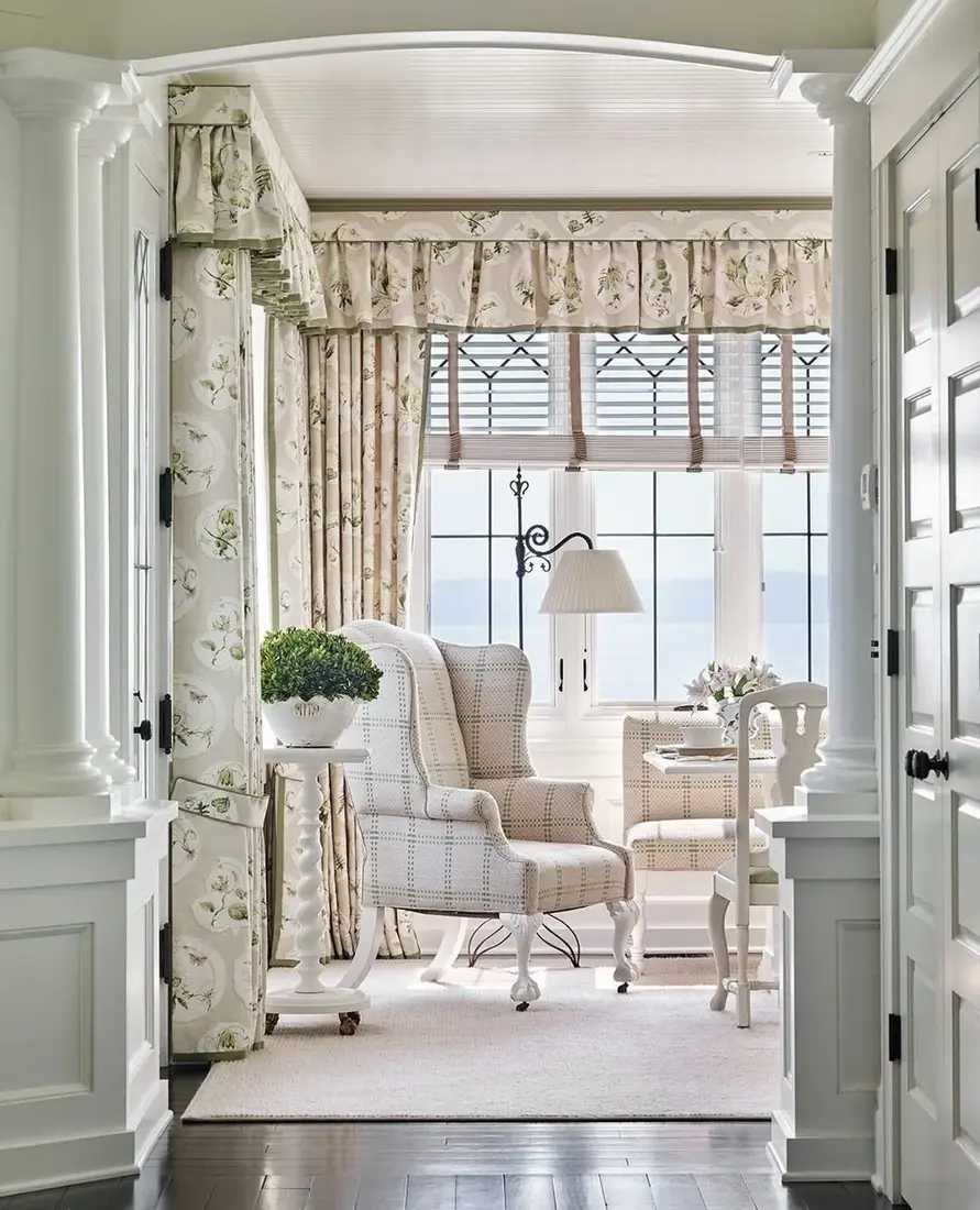 Narrow white nook with checked wing chair, roman blind, and layered curtains