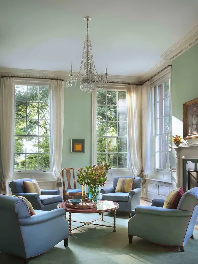 Sage sitting room with four blue armchairs, tall sashes, and sheers