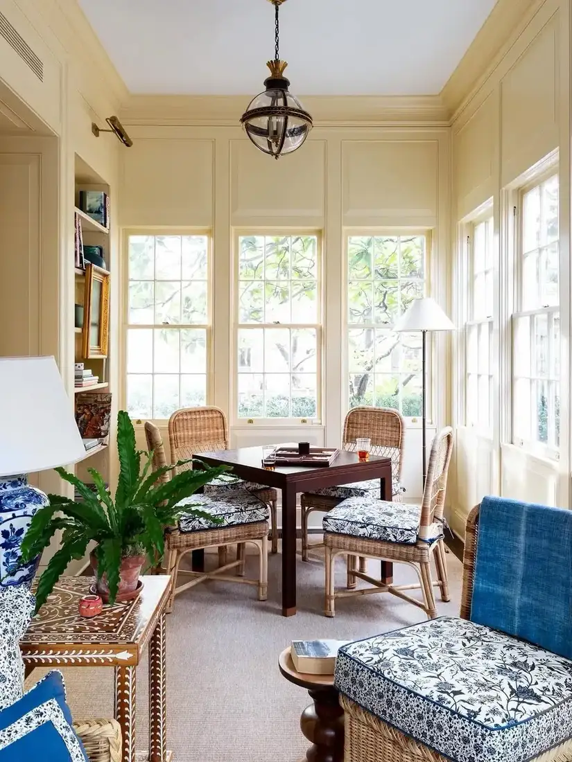 Butter yellow sunroom with cane chairs, dark game table, and blue cushions