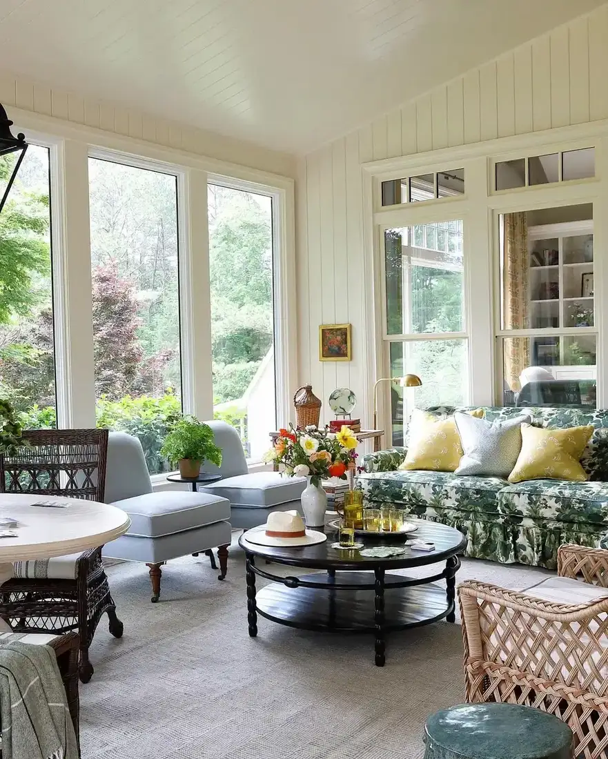 Sunroom with green floral chintz sofa, pale chairs, and tall windows