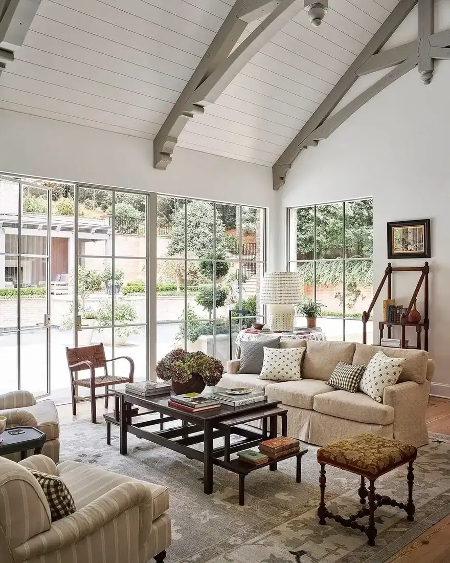 Vaulted sitting room with grey trusses, steel windows, and linen seating