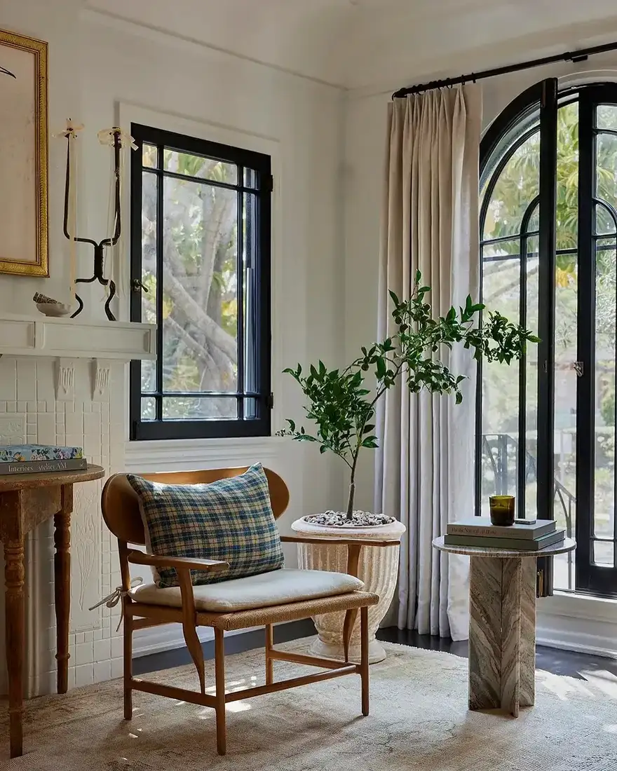 White sitting room with black arched steel doors, cane chair, and citrus tree