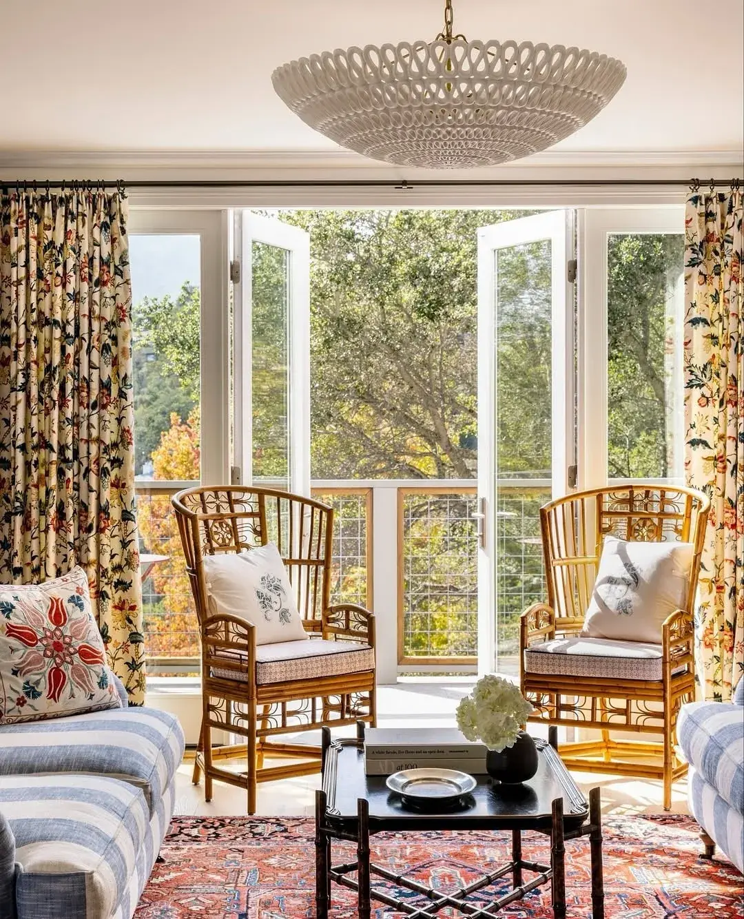 Cream floral curtains on a slim dark rod spanning a wall of open French doors under a woven ceiling light