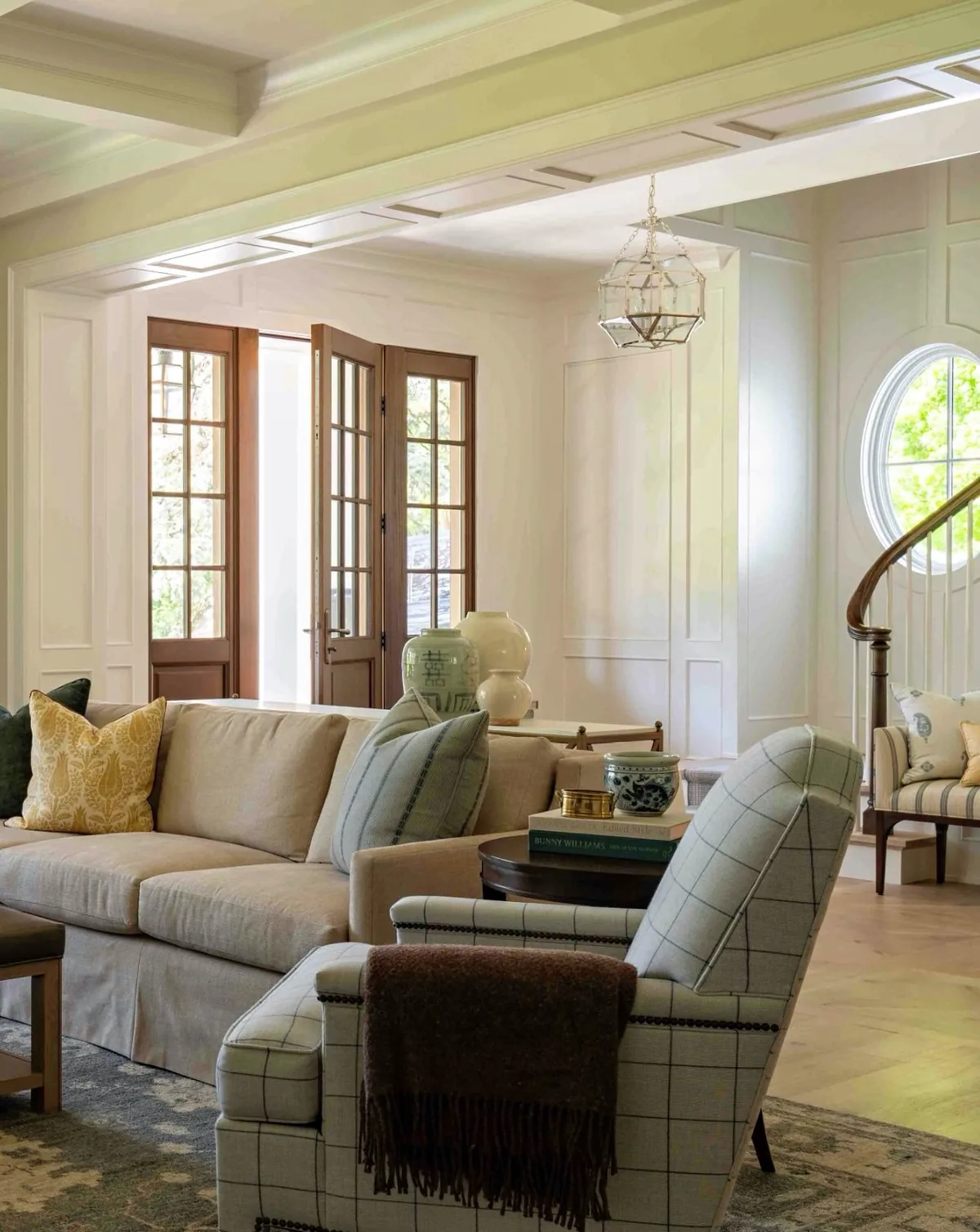 Cream living room with a green windowpane check chair and timber French doors folded flat against the wall