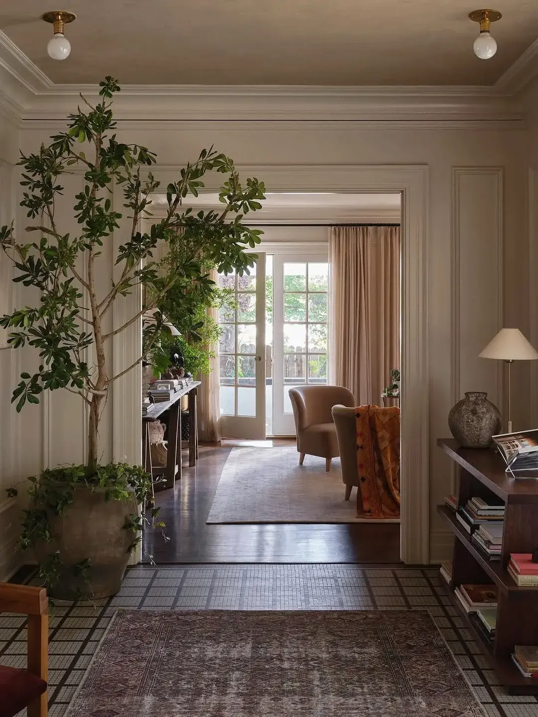 Entry hall with a large potted tree, a vintage rug on tiled floor and a view through to French doors