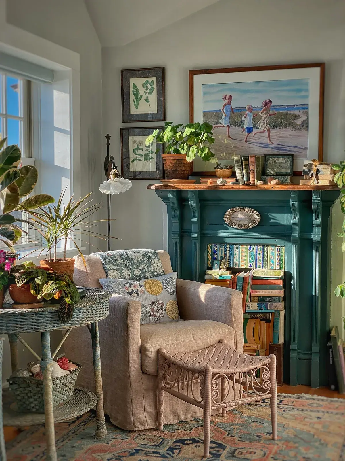 Armchair and footstool beside a window, with books stacked in a disused teal fireplace