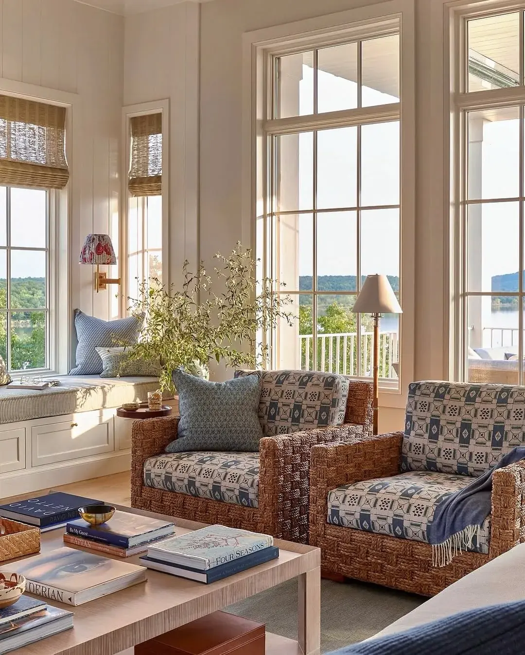 Window seat with blue cushions beside rattan chairs overlooking water