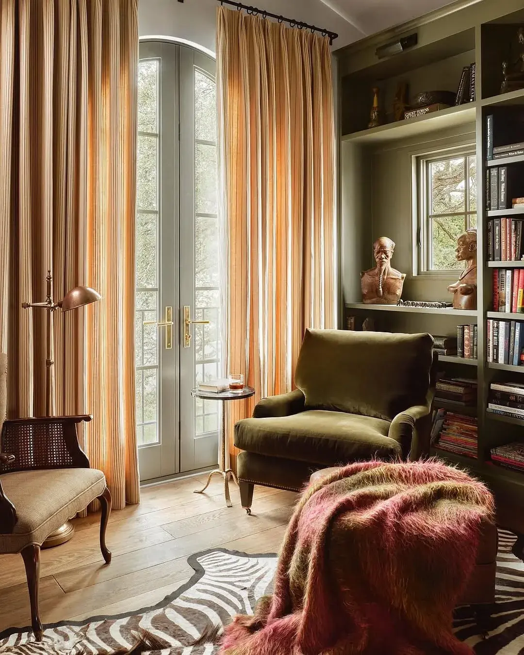 Olive velvet armchair beside French doors with striped curtains