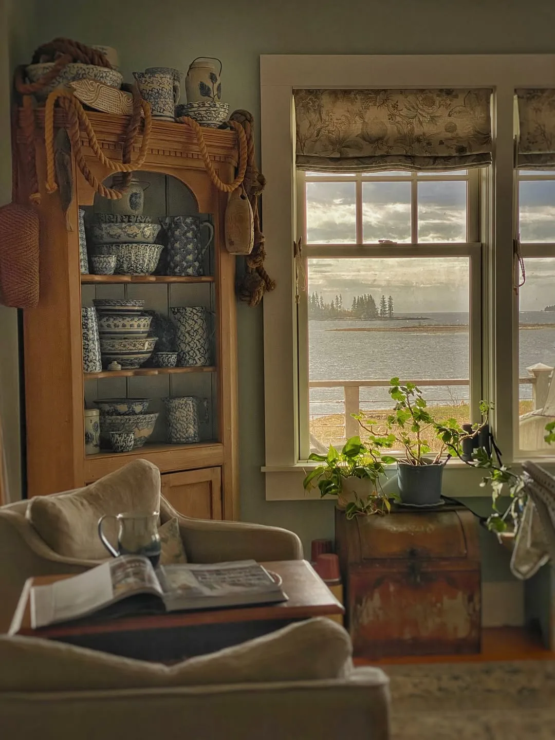 Armchair with open book facing sea view beside pine dresser